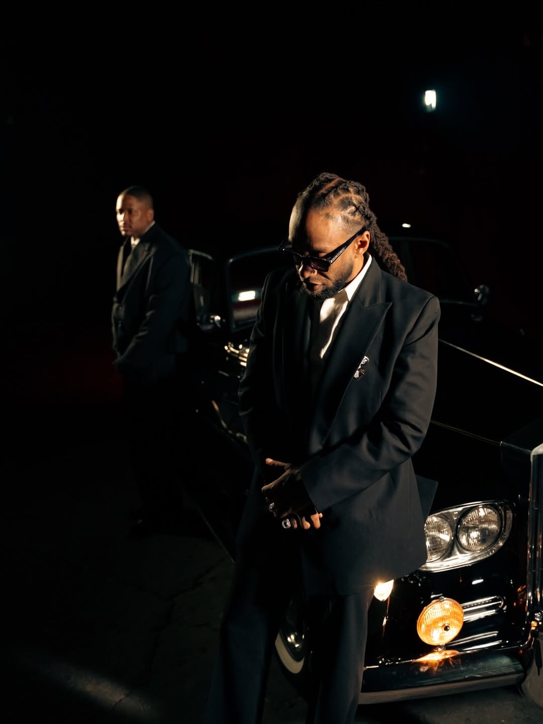 A man standing beside a classic Rolls-Royce during a music video shoot.