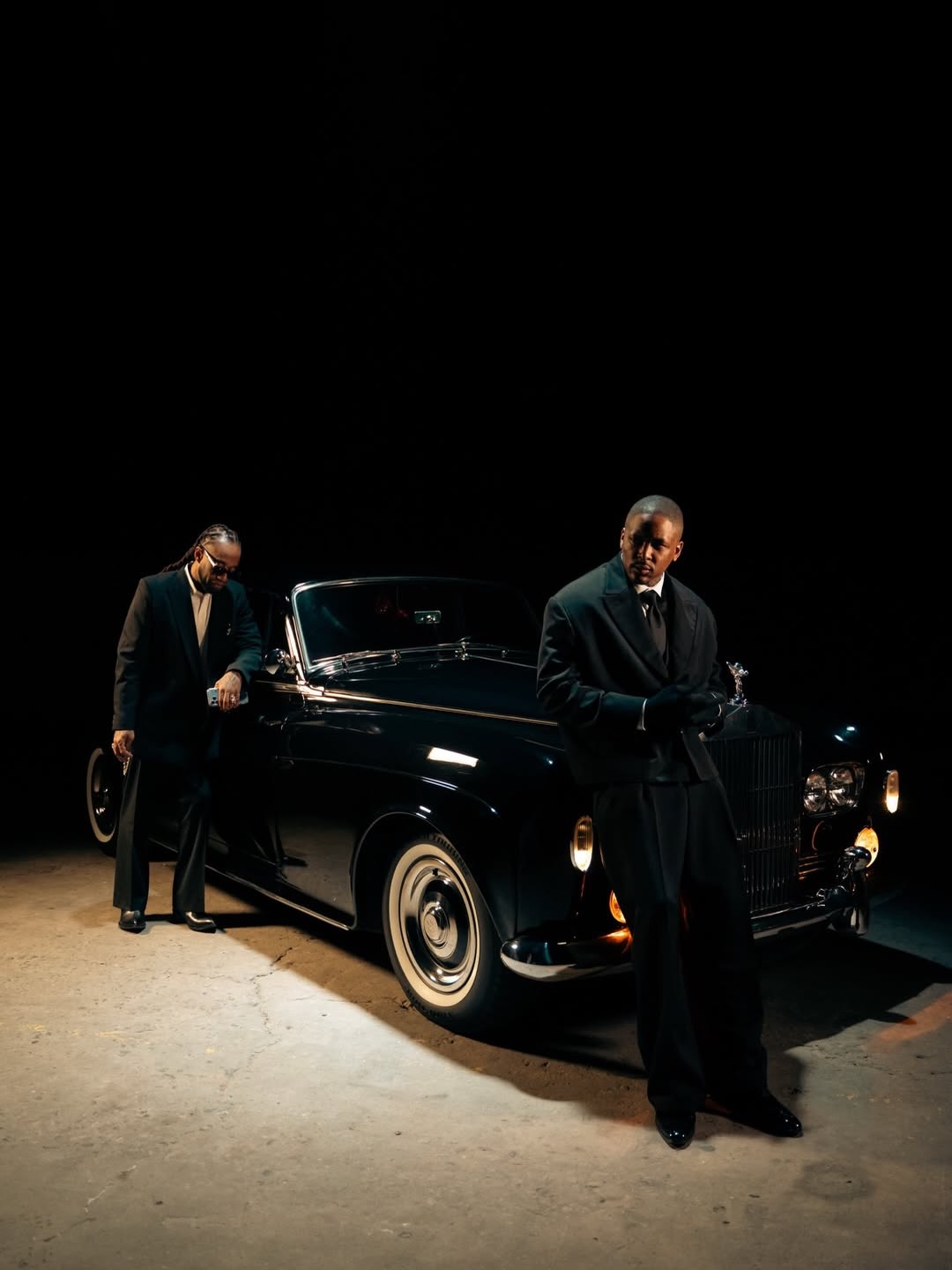 A man in front of a classic Rolls-Royce at a nighttime production.